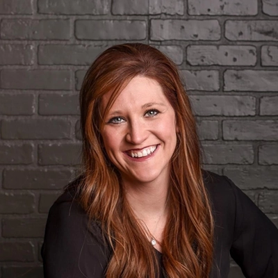 Dr. Sarah Cook with her hair down and a big smile, standing in front of a black brick background.